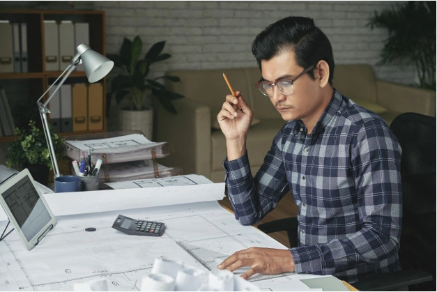 homem de camisa xadrez cinza e azul sentado a uma mesa estudando como viver de renda e como calcular seus investimentos