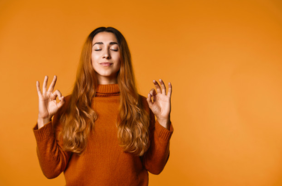 garota ruiva com suéter laranja a frente de parede laranja mais calara com os olhos fechados e mãos levantadas